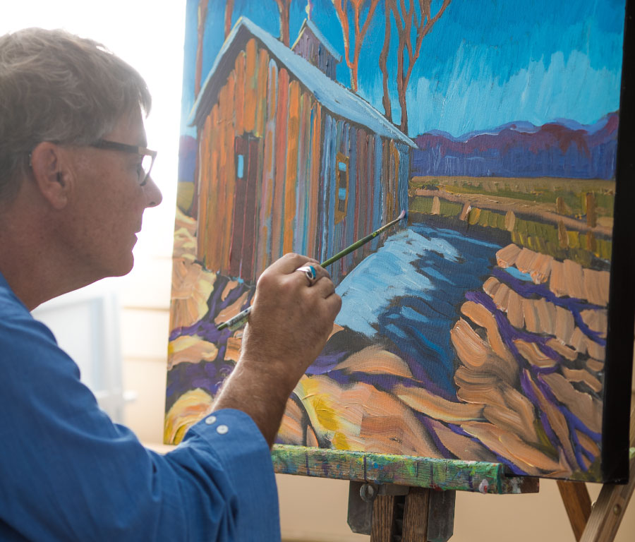 Photo of Strachan Johnston while painting The artist at work, painting a colourful barn and landscape